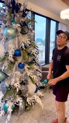 a man standing next to a white christmas tree in an office building with blue and silver ornaments on it