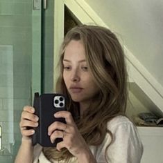 a woman taking a selfie with her cell phone in front of her and looking into the mirror