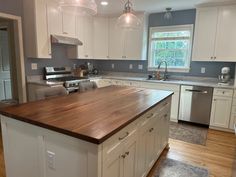 a large kitchen with white cabinets and wood counter tops on the island in front of the sink