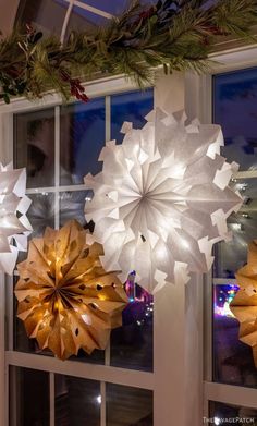 three paper snowflakes hanging from the ceiling in front of a window at night