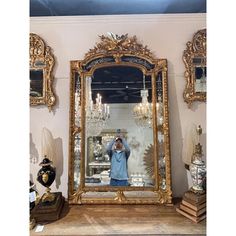 a man taking a selfie in front of a large gold mirror with chandelier