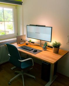 a desk with a computer, phone and potted plant on it in front of a window