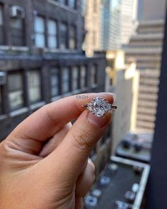 a woman's hand holding an engagement ring in front of a cityscape