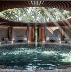 an indoor swimming pool surrounded by lounge chairs and palm trees in the background with sunlight streaming through