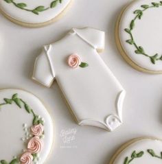 cookies decorated with baby clothes and flowers are arranged on a white tablecloth next to some cookies