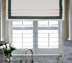 a kitchen sink under a window with roman shades