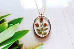 a necklace with pressed flowers in it on a wooden table next to green plant leaves