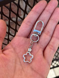 a hand holding a metal keychain with a flower on it