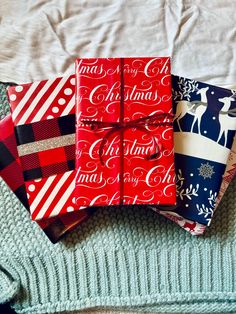 three wrapped christmas gifts sitting on top of a bed next to a sweater and pillow