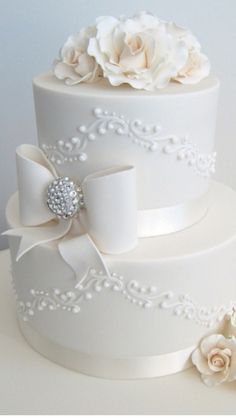 a three tiered white wedding cake decorated with flowers and pearls, on a table