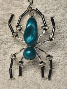 a blue spider pendant with black beads on it's back legs and arms hanging from a silver chain