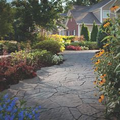 a stone path in front of a house surrounded by flowers