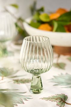 an empty glass sitting on top of a table next to a bowl of oranges