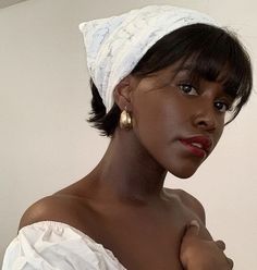 a woman wearing a white head wrap and gold hoop earrings is posing for the camera