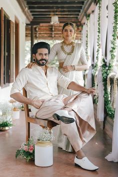 a man and woman sitting on a chair in front of a doorway with greenery