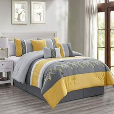 a bed with yellow and gray comforters in a room next to a white dresser