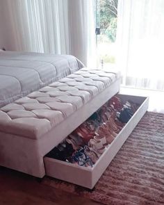 a white bed with drawers underneath it on the floor in front of a large window