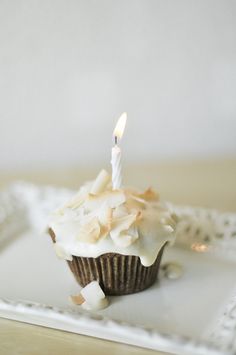 a cupcake with a lit candle on it sitting on a white plate in front of a wall