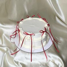 a white cake with red ribbon and bow on it sitting on a satin tablecloth