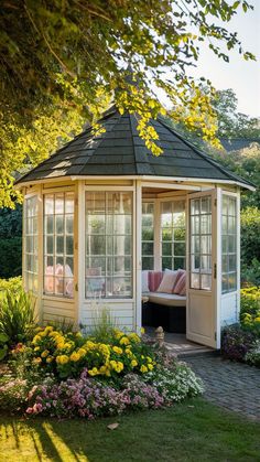 a small gazebo in the middle of a garden with flowers and plants around it