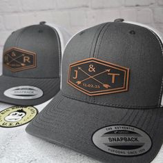 two gray and white hats with brown patches on them, one is for the trucker