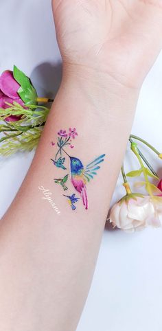 a small tattoo on the wrist of a woman's arm with hummings and flowers