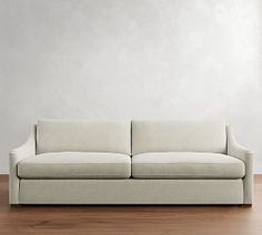 a white couch sitting on top of a hard wood floor next to a wall in an empty room