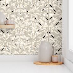 two white vases sitting on top of a counter next to a wall with geometric designs