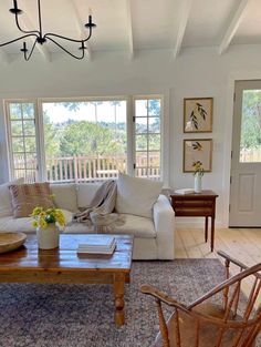 a living room filled with furniture and a wooden table in front of two large windows