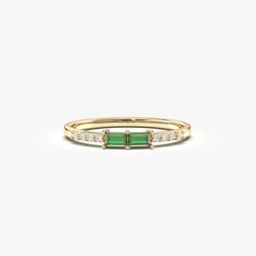 a yellow gold ring with emerald and white diamonds on the sides, set against a plain background