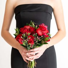 a woman in a black dress holding a bouquet of red roses