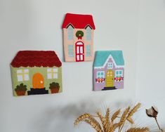 three felt houses hanging on the wall next to a vase with dried flowers in it