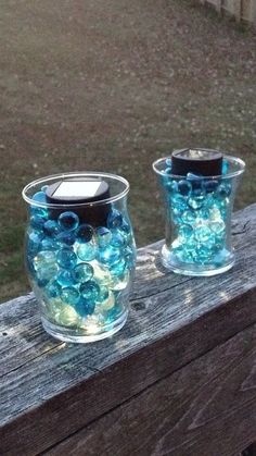 two glass vases filled with blue and green beads sitting on a wooden fence post