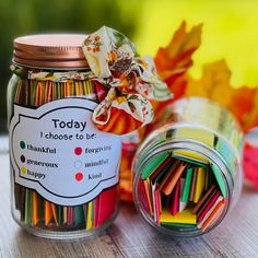 a jar filled with colored pencils sitting on top of a table next to leaves