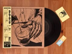 a record with a hand holding a glass in it on top of a wooden table