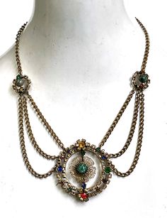 Vintage Necklace Czech Festoon Multi color stones This is a Spectacular Vintage Czech festoon style necklace made of brass filigree and colorful Czech glass stones. I think that this necklace dates to the 1920s or 1930s, it has an Egyptian revival style with double brass filigree rings accented with red, blue, green, purple .and yellow sparkling prong set glass stones with brass flowers. There is a brass filigree flower in the center with a green speckled glass stone in the center. On either side of the center pendant,  there are three swagged brass chains on each side that meet at a smaller brass filigree flower and lead to single brass chain that wraps around the neck and closes with a spring ring clasp. Measures 18" , pendant measure 2 1/8" x 2 1/8". This stunning antique piece is a rar Filigree Rings, Brass Flowers, German Jewelry, Czech Jewelry, Festoon Necklace, Brass Filigree, Vintage Jewelry Sets, Color Stones, Egyptian Revival