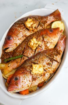 some fish are in a white bowl with lemons and seasonings on it,