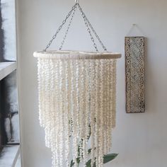 a large white beaded mobile hanging from a wall next to a potted plant