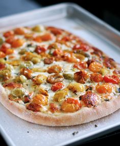 a pizza sitting on top of a pan covered in cheese and toppings with tomatoes