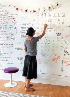 a woman writing on a whiteboard with markers and pens in front of the wall