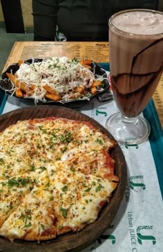 a pizza sitting on top of a wooden pan next to a glass of milkshake