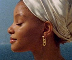 a woman with a turban on her head and earring in front of a blue wall