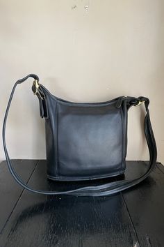 Here we have a simply stunning vintage Coach Slim Duffle bag. Comes with an original hang tag. I'm obsessed with this design. Pocket on the front of the bag. Zipper top with leather pull. The inside is very clean with a very open inside and one pocket. Serial is NO E9C-9816. The leather does show some wear and does have some spots. Please see the pictures.  The bag has been treated with leather CPR. Glovetanned leather, Inside multifunction pocket, Zip-top closure, leather lining, and Outside sl Classic Crossbody Bucket Bag With Leather Lining, Classic Tote Bucket Bag, Classic Shoulder Bucket Bag With Leather Lining, Vintage Black Hobo Shoulder Bag, Classic Leather Lined Crossbody Bucket Bag, Classic Leather-lined Shoulder Bucket Bag, Black Vintage Hobo Shoulder Bag, Vintage Black Rectangular Shoulder Bag For Everyday Use, Vintage Black Hobo Bag For Daily Use