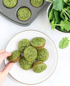 a person picking up some green muffins on a plate with spinach leaves in the background