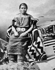 an old black and white photo of a woman in native clothing sitting on a hill