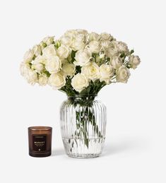 white roses in a glass vase next to a candle