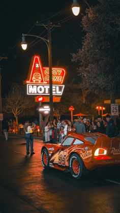 a car parked in front of a motel sign at night with people standing around it