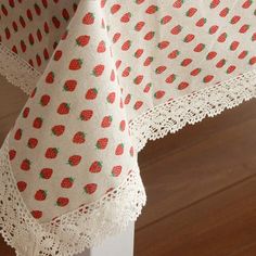 the table cloth has strawberrys on it and is white with red dots, along with a lace edge