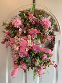 a wreath hanging on the front door decorated with pink flowers and greenery is adorned with a pink ribbon