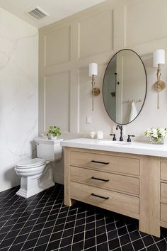 a white toilet sitting next to a bathroom sink under a round mirror on top of a wooden cabinet